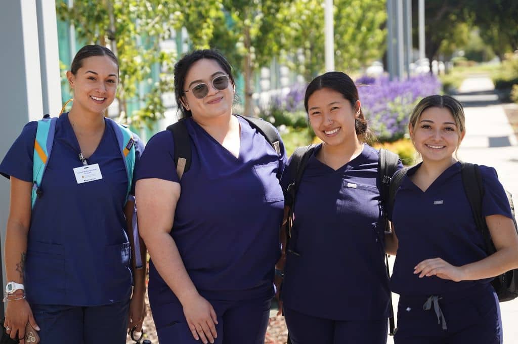 Group of students in scrubs smiling on campus, showcasing community and support in medical billing and coding certification programs in Texas.