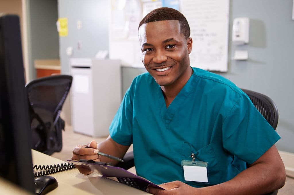 Smiling healthcare worker in scrubs at a computer, representing career opportunities after earning a medical billing and coding certification in Texas.