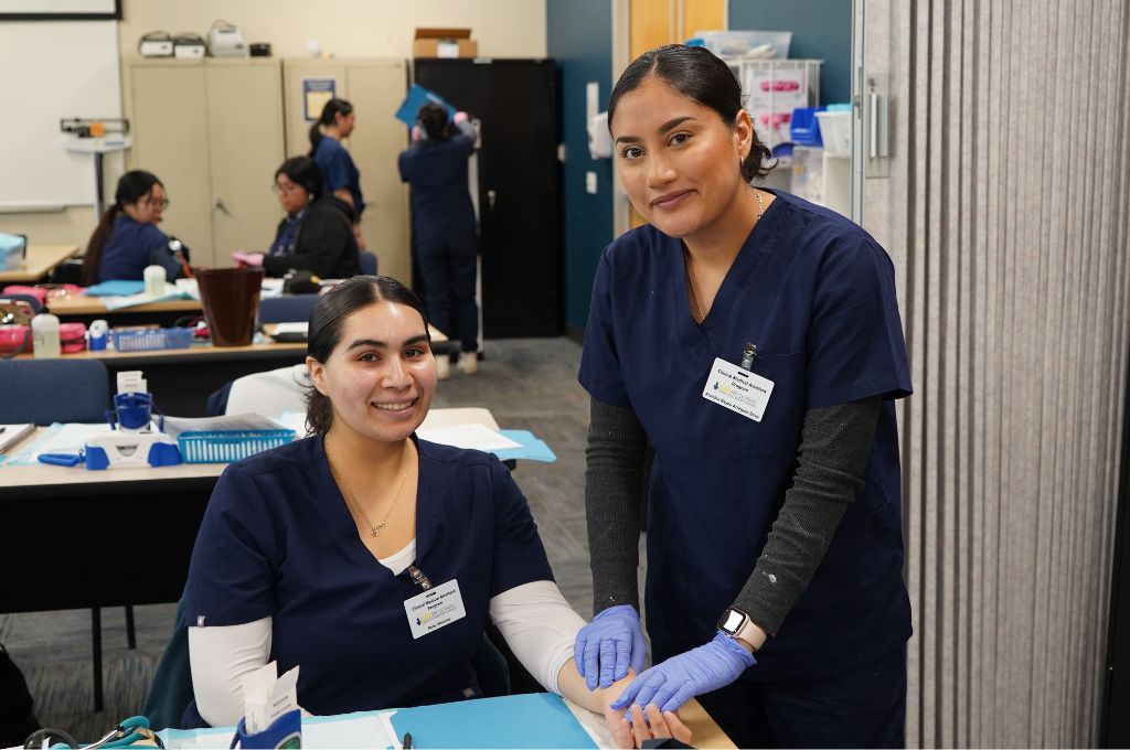 Medical assistant students performing a practical lab activity, highlighting real-world patient care responsibilities outlined in the medical assistant job description.