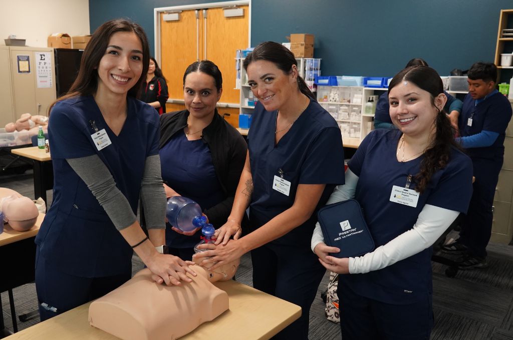 Four CALRegional medical assistant students practicing CPR on a mannequin during in-person training.