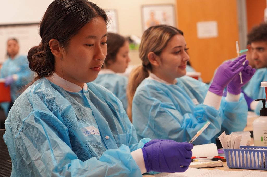 CALRegional medical assistant students in blue gowns preparing injections as part of their clinical skills lab.
