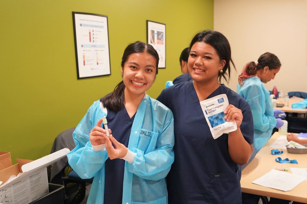 Phlebotomy training students smiling in lab class holding a blood sample tube